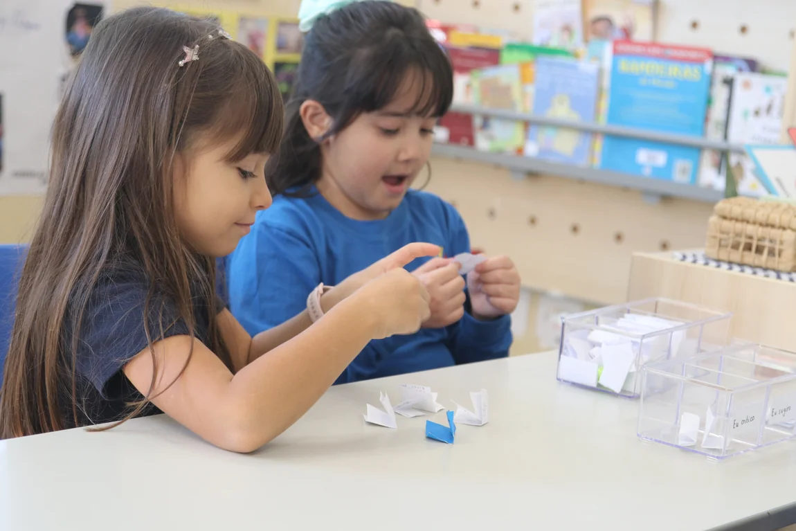 Duas alunas do Múltiplo International School manipulando material concreto sobre a mesa, numa sala do Fundamental Anos Iniciais