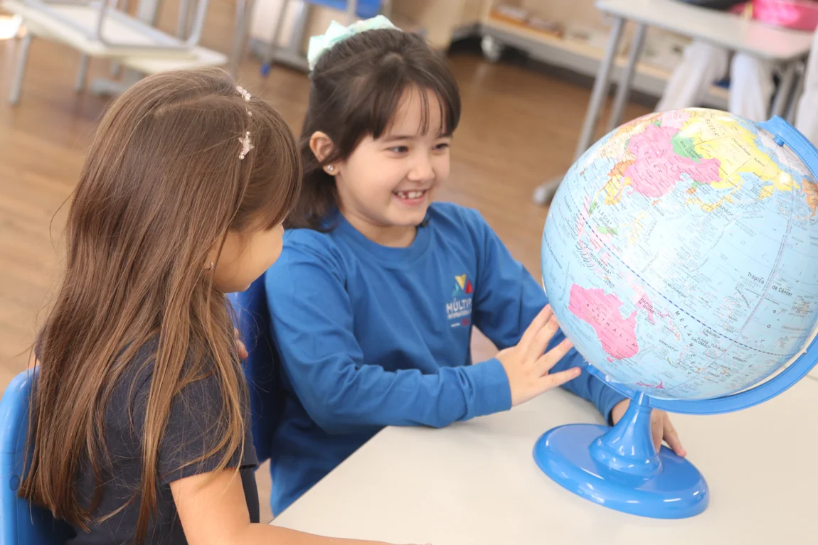 Duas alunas do Múltiplo International School explorando um globo terrestre numa sala do Fundamental Anos Iniciais