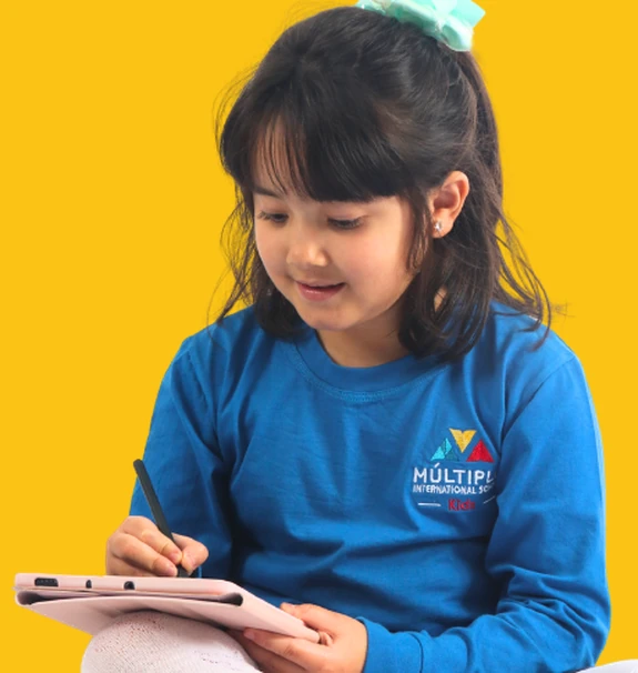 Aluna do Múltiplo International School sentada no chão, escrevendo num tablet com caneta, sobre fundo amarelo
