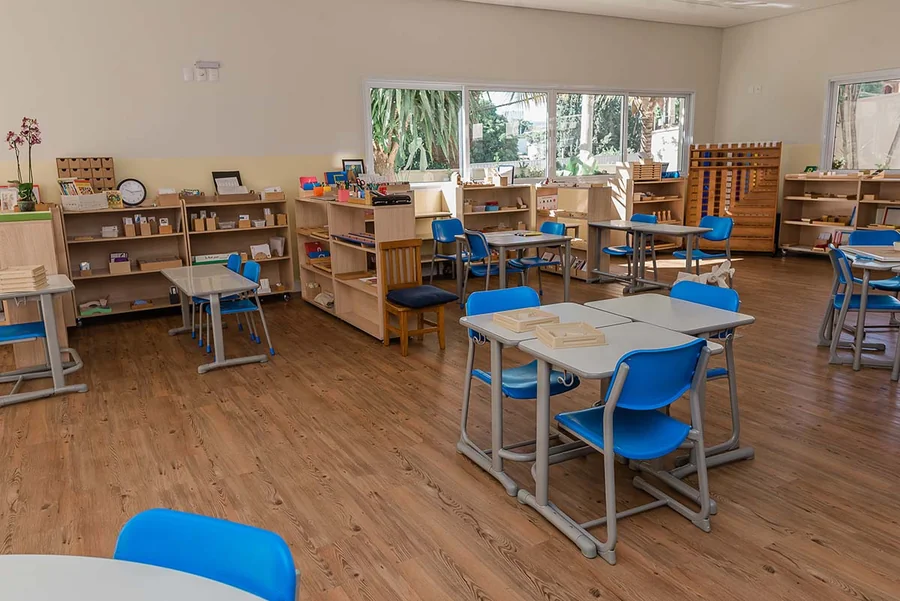Sala Montessori da unidade Kids do Múltiplo, com mesas baixas, cadeiras azuis e estantes de material concreto