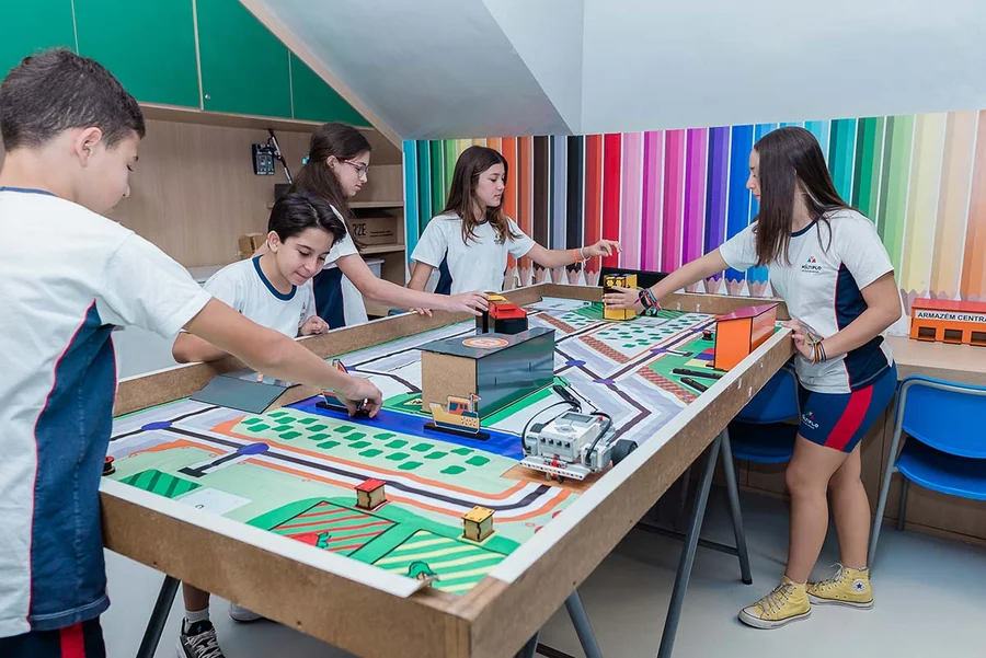 Sala de atividades do Múltiplo, com alunos em volta de um tabuleiro grande sobre as mesas
