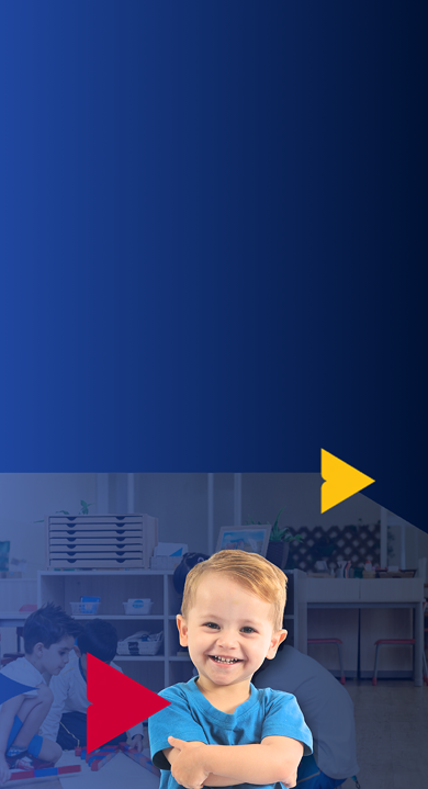 Aluno da Educação Infantil do Múltiplo International School de braços cruzados, sorrindo, numa sala Montessori com outras crianças ao fundo